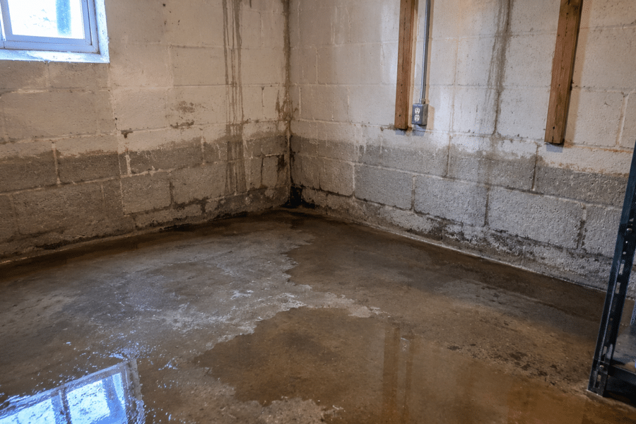 Basement corner with visible water pooling and wall staining indicating moisture intrusion after heavy rain