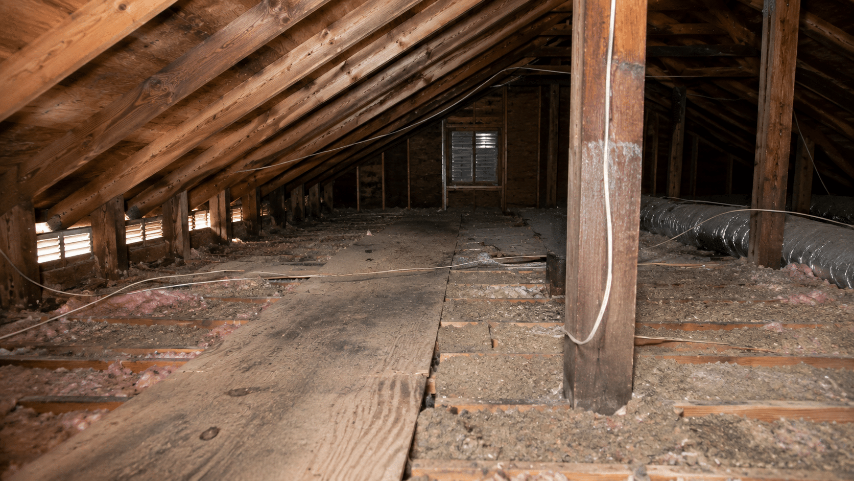 Residential attic with exposed rafters, aged insulation, and visible roof ventilation during a home inspection